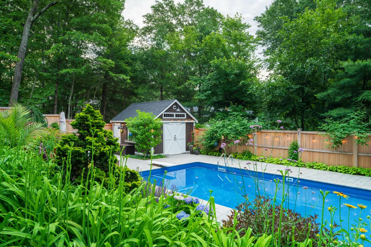 Custom backyard pool and landscape design in Middlesex County MA with vibrant flower beds, stonework, and patio seating.