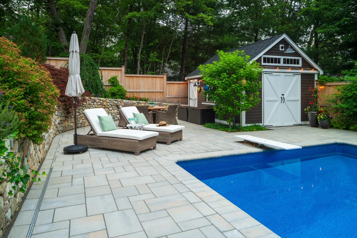 Custom backyard pool and landscape design in Middlesex County MA with vibrant flower beds, stonework, and patio seating.