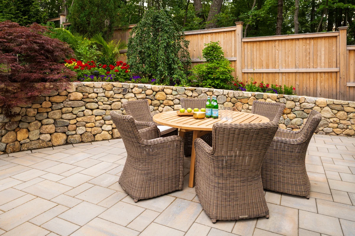 Outdoor dining area with wicker chairs and natural stone wall, part of a professional landscape design project in Middlesex County Massachusetts.