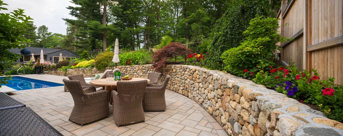 Outdoor dining area with wicker chairs and natural stone wall, part of a professional landscape design project in Middlesex County Massachusetts.
